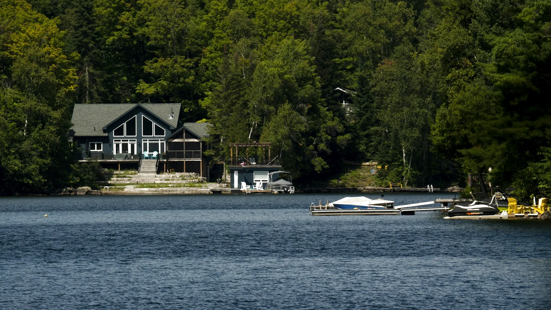 A lakefront home with large windows, a deck and a dock, surrounded by trees.