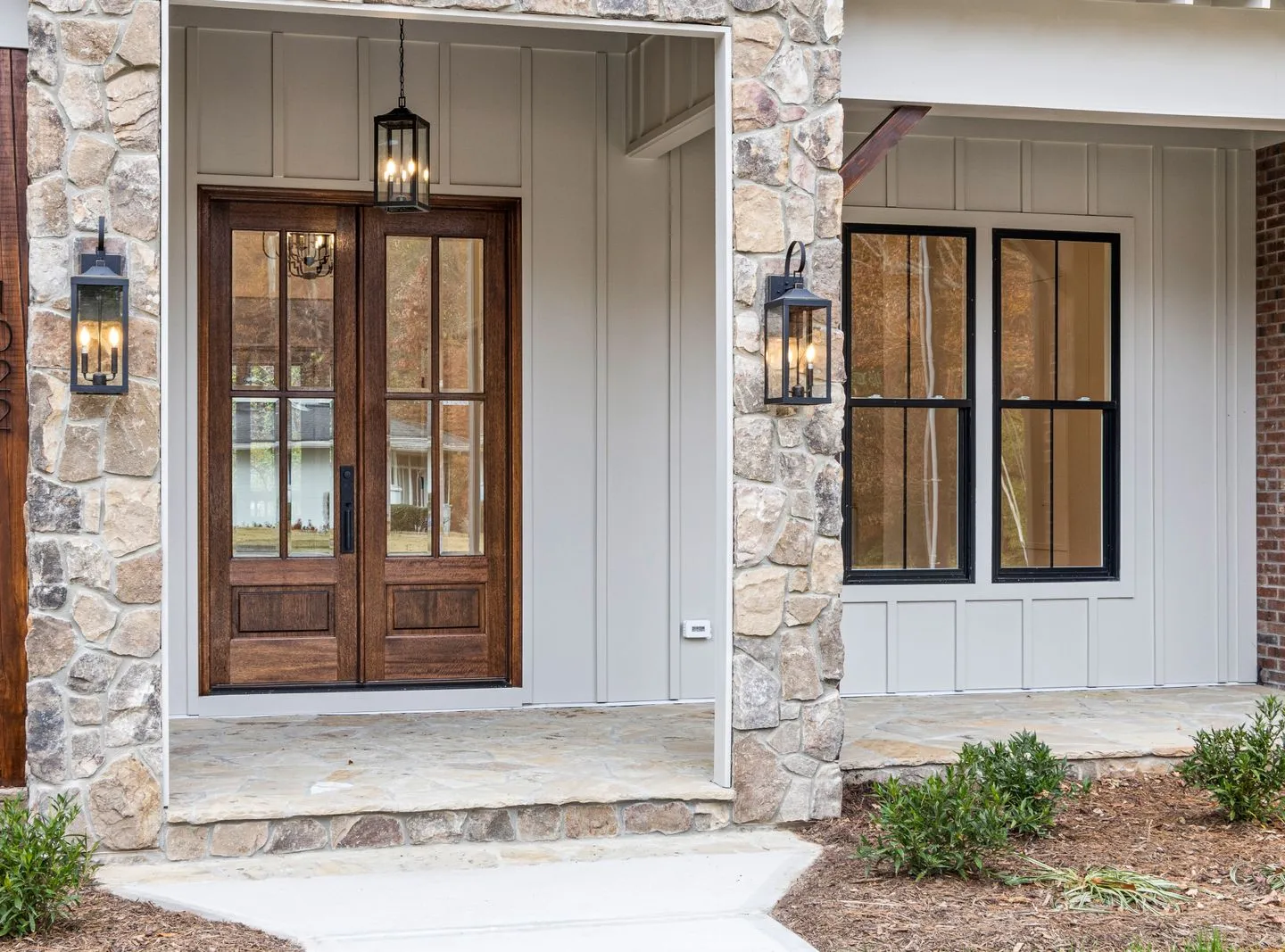 A welcoming timber front door framed by stone columns and warm porch lights.